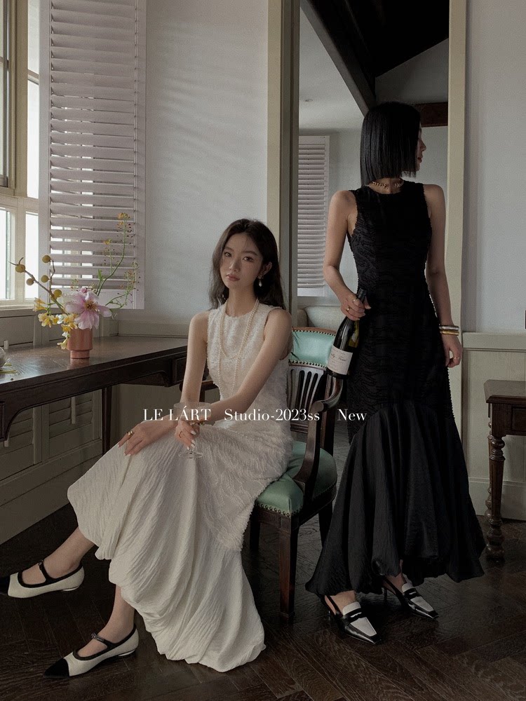 Two models wearing elegant black and ivory sleeveless dresses in a studio setting