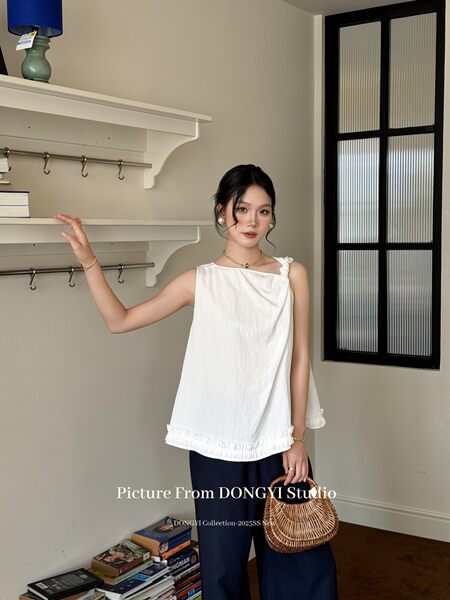 Model wearing a white sleeveless ruffled top with dark wide-leg pants and a woven handbag