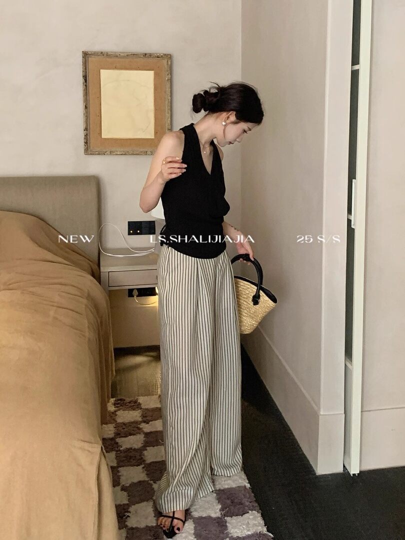 Woman wearing a black sleeveless top with striped wide-leg pants and carrying a straw handbag