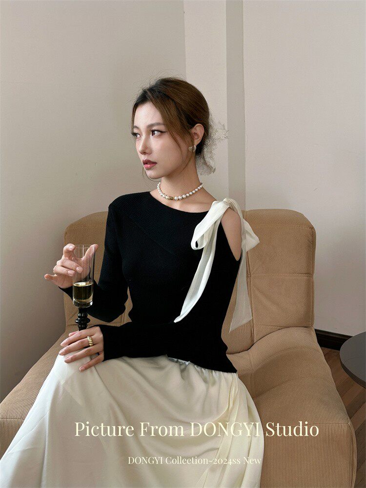 Woman wearing a black off-shoulder top with white ribbon detail and a cream skirt