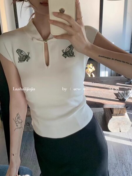 Woman wearing a cream sleeveless top with butterfly embroidery and a small keyhole neckline