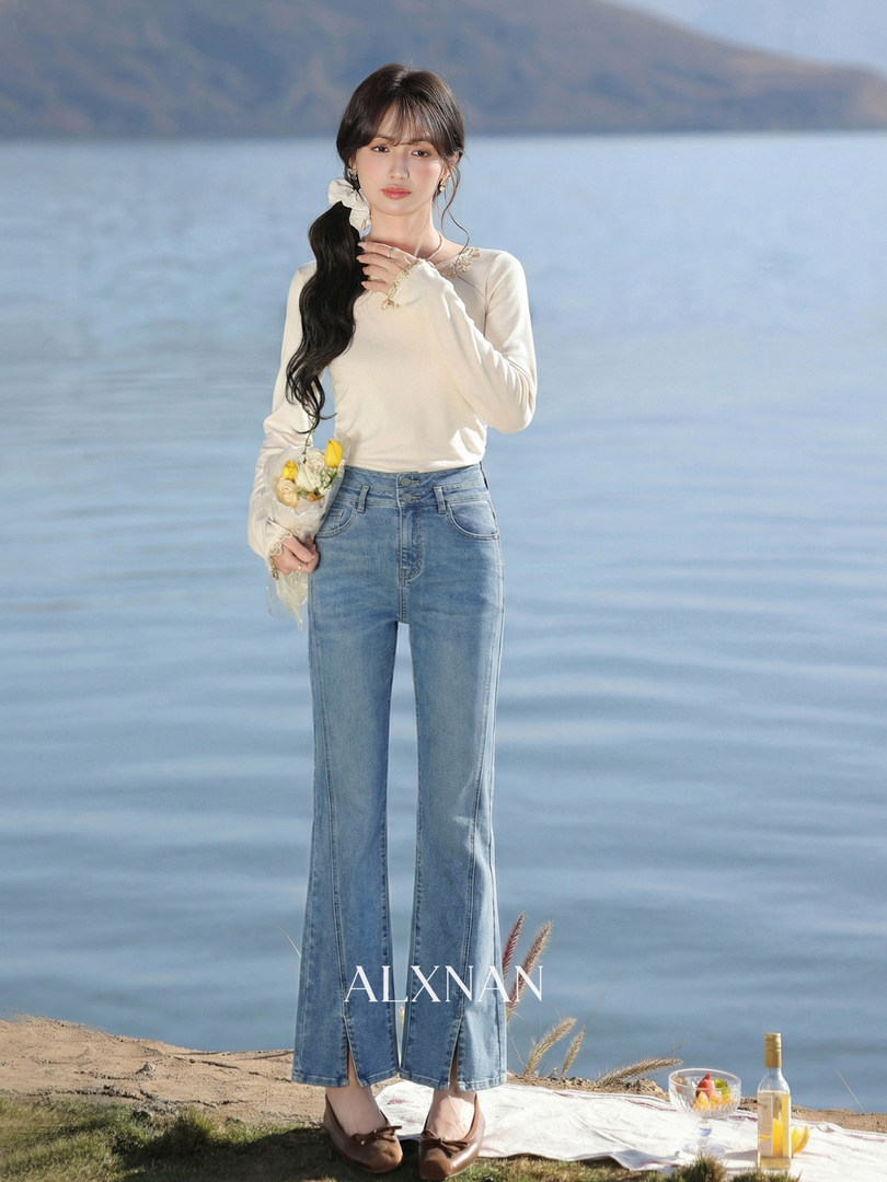 Woman wearing a cream long-sleeve top and light blue flared jeans by the water