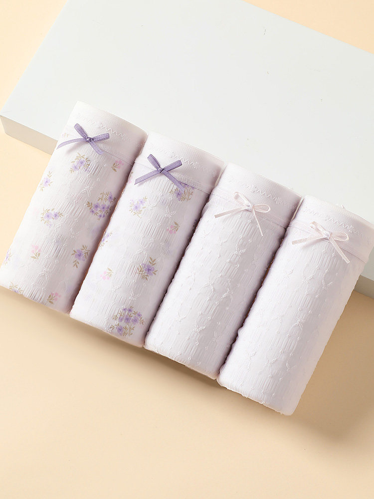 Four folded pastel women’s underwear briefs with small bows on a light background