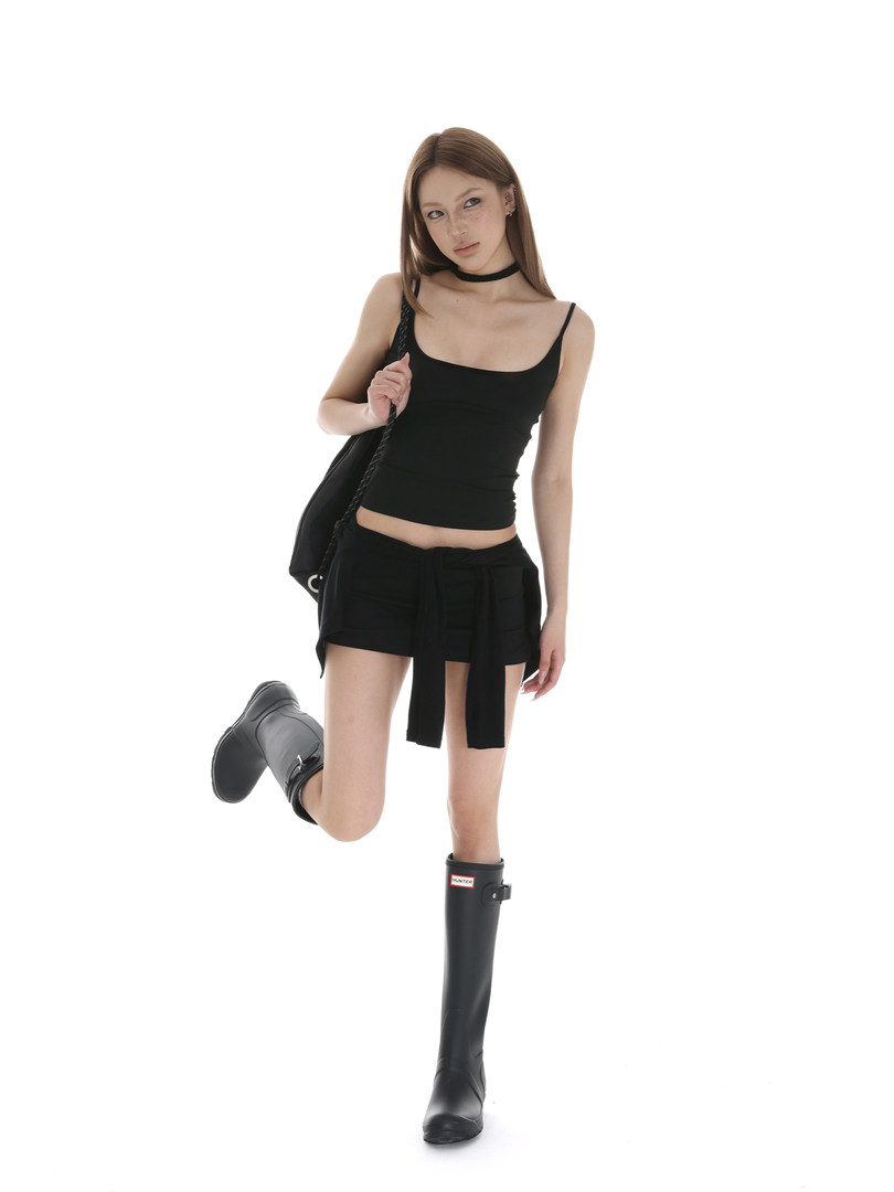 Model wearing a black tank top, mini skirt, and tall black boots on a white background
