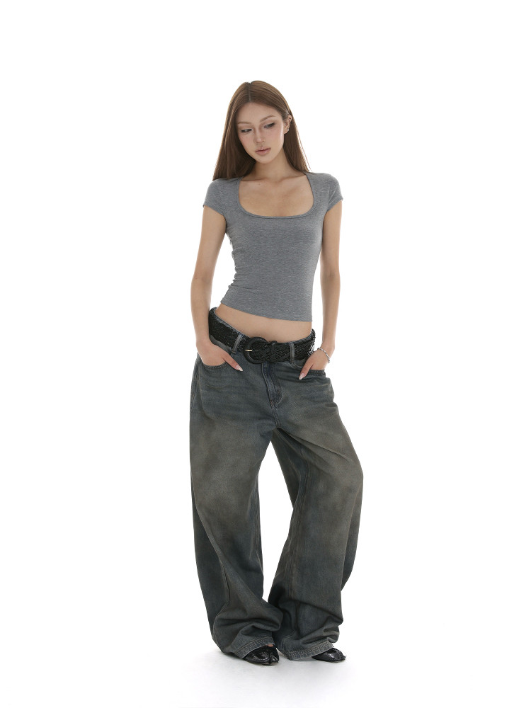 Female model wearing a gray fitted top with baggy dark jeans on a white background