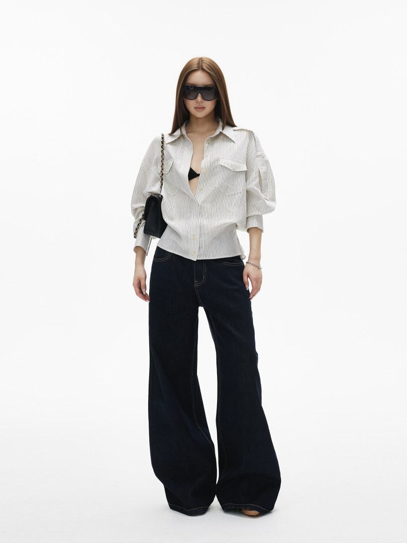 Model wearing a white striped button-up shirt with black wide-leg pants and sunglasses