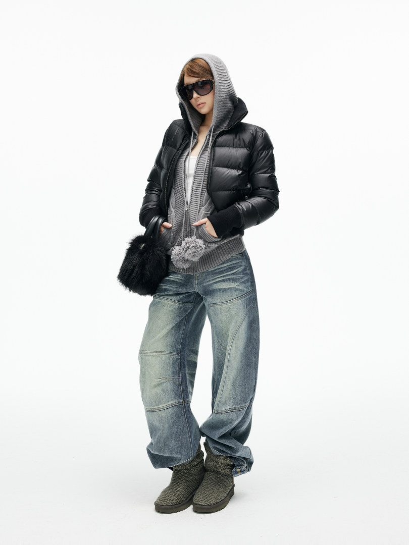 Model wearing a hooded black puffer jacket, gray knit hoodie, wide-leg jeans, and boots