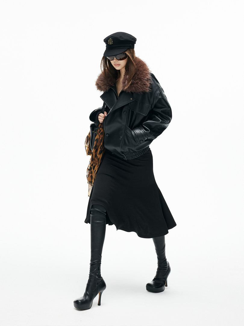 Model wearing a black leather jacket with faux fur collar, black skirt, boots, and cap