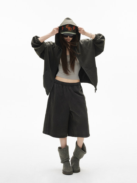 Model wearing an oversized dark hoodie, wide shorts, and knit boots on a white background