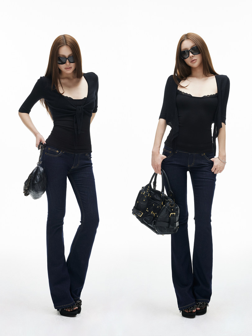 Model wearing a black fitted top with dark jeans and holding a black handbag