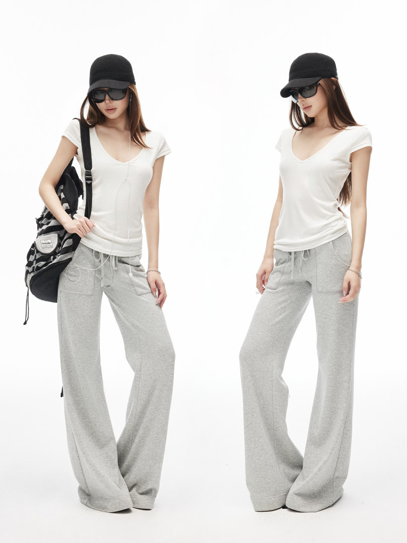 Model wearing a white fitted top and gray wide-leg sweatpants with cap and sunglasses