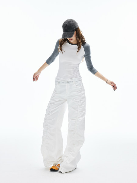 Model wearing white wide-leg pants with a gray-and-white raglan top and dark cap