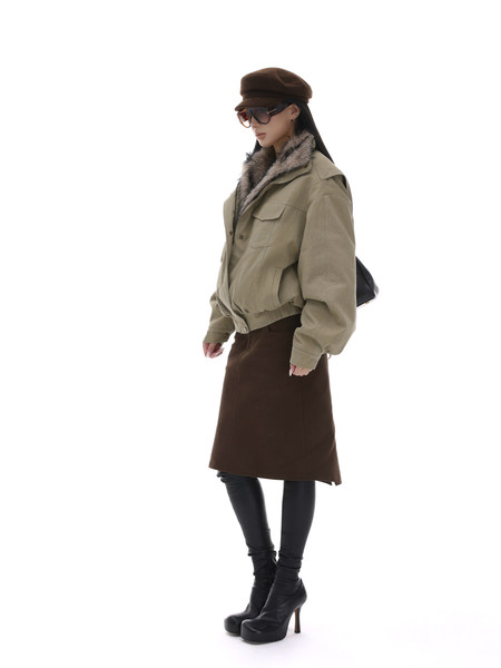 Fashion model wearing a beige jacket, brown skirt, black leggings, boots, and a brown cap