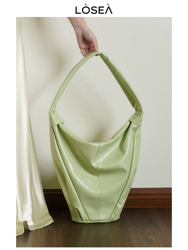 Light green oversized shoulder handbag held by hand on a neutral background