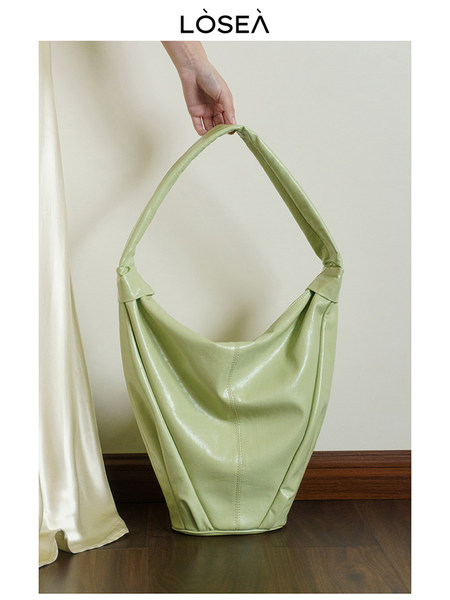 Light green oversized shoulder handbag held by hand on a neutral background