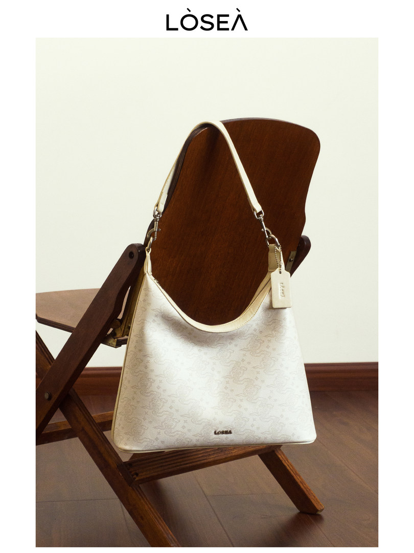 Cream shoulder handbag with a white strap displayed on a wooden chair