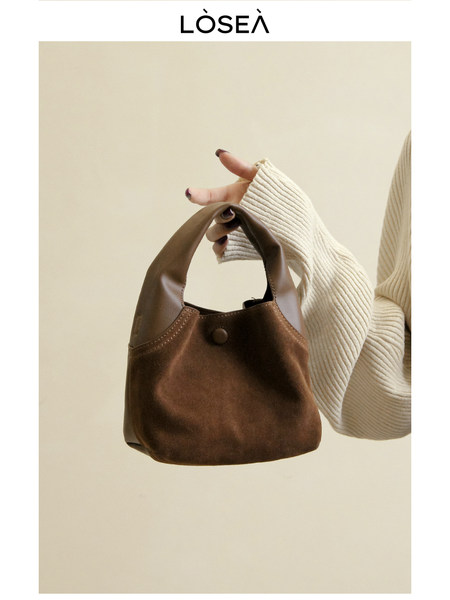 Brown leather handbag held by a person against a plain background