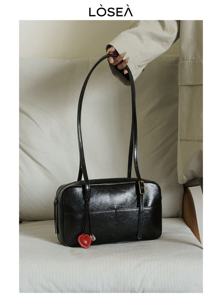 Black leather shoulder handbag with long strap and heart charm on a chair