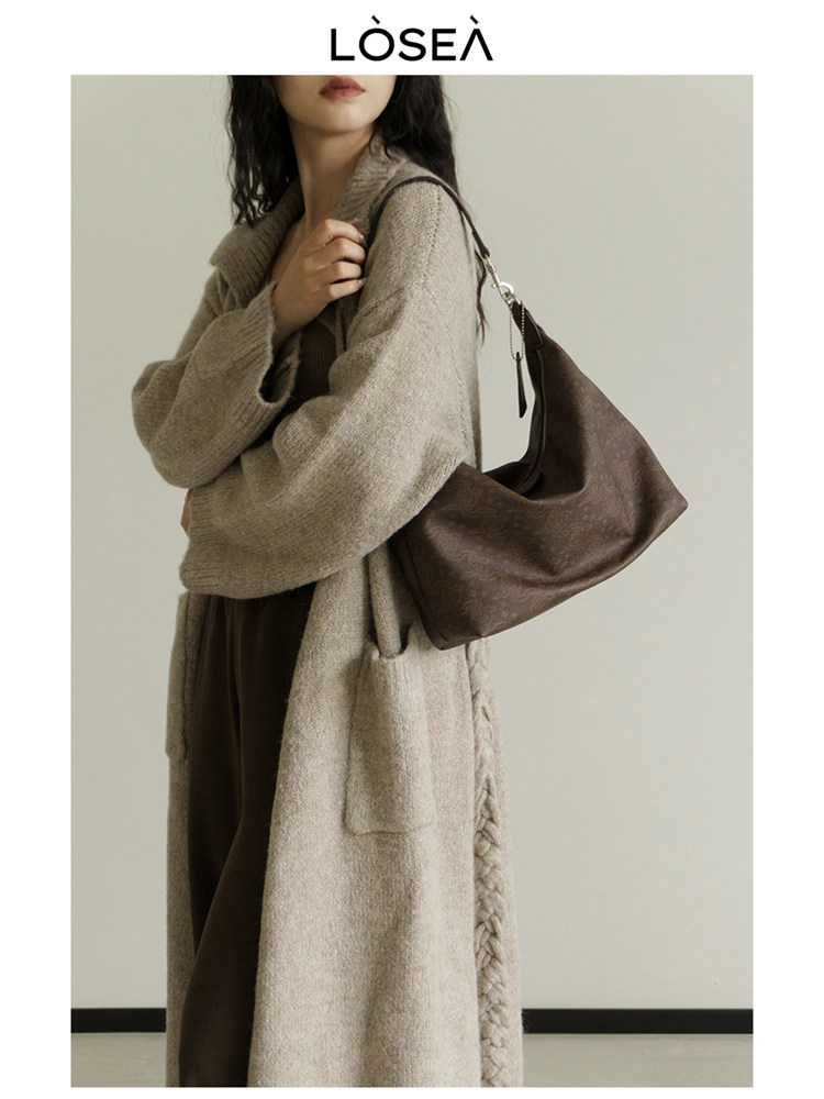 Model wearing a long beige knit coat with a brown shoulder bag