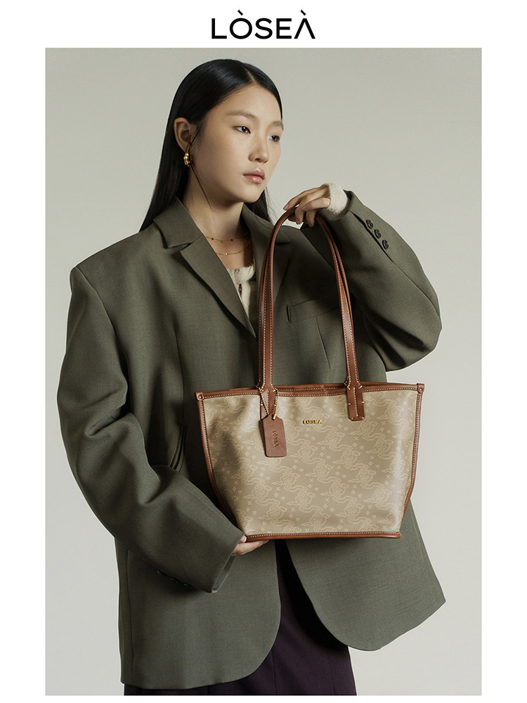 Model holding a beige patterned tote bag with brown handles and trim