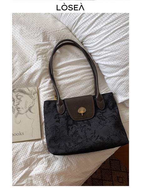 Black floral-pattern tote handbag with brown handles and flap closure