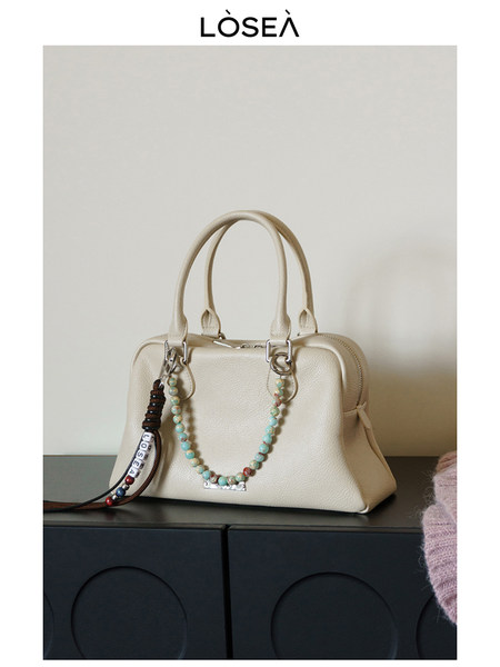 Cream leather handbag with top handles and beaded charm on display