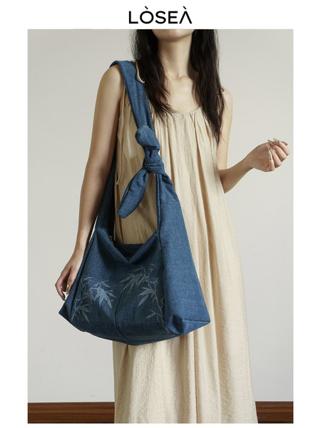 Blue denim-style shoulder bag worn by a model in a beige dress