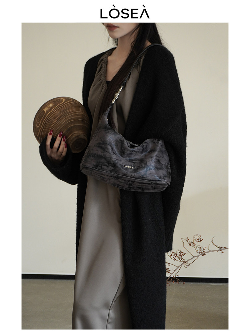 Model wearing a dark shoulder handbag with a black cardigan and neutral dress