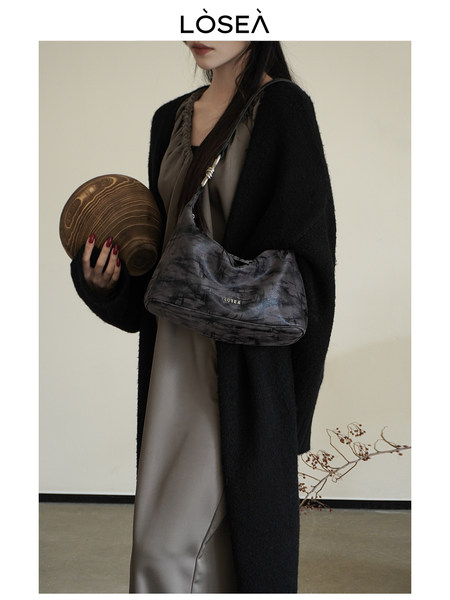 Model wearing a dark shoulder handbag with a black cardigan and neutral dress