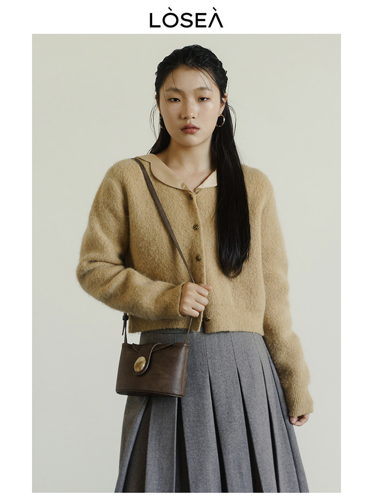 Model wearing a tan fuzzy cardigan with a gray pleated skirt and small brown crossbody bag