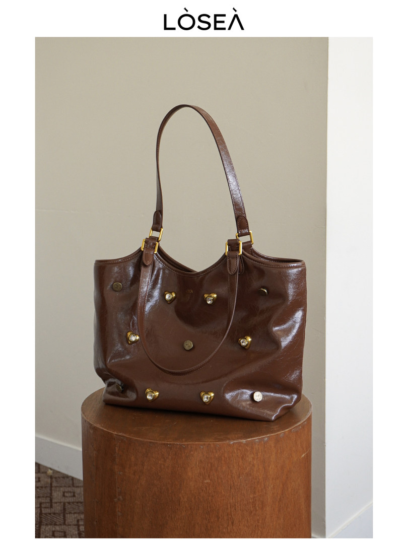 Brown leather tote handbag with gold hardware on a stand