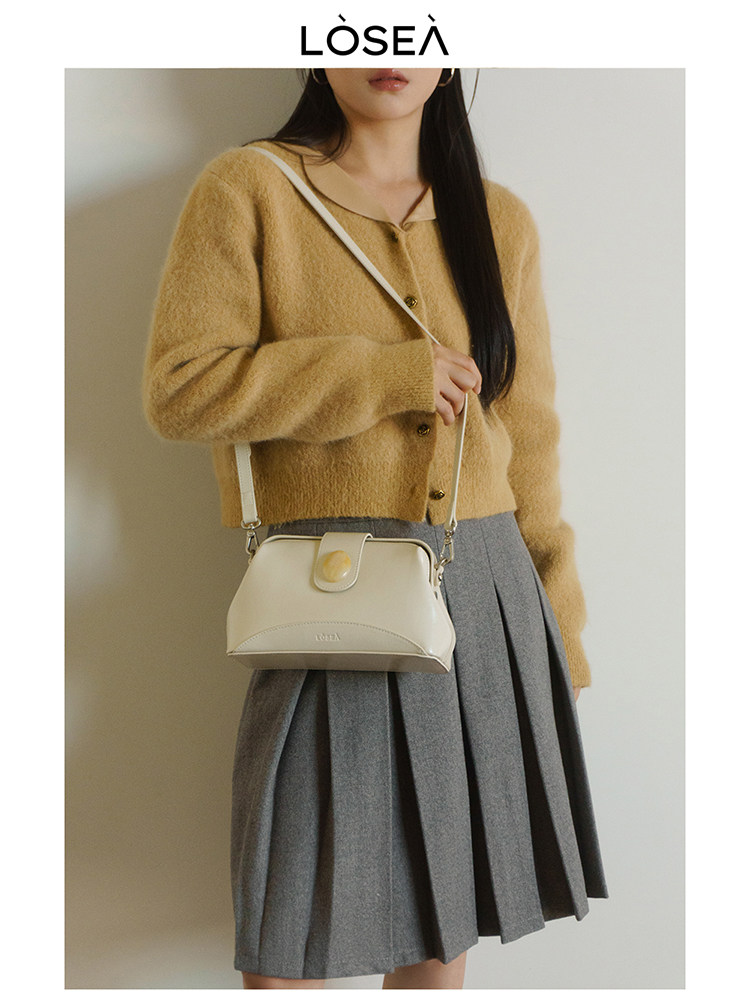 Cream shoulder handbag worn with a mustard cardigan and gray pleated skirt