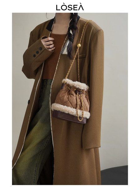 Model wearing a brown long coat with a quilted bucket bag