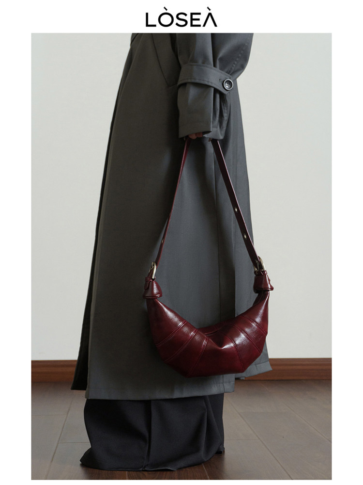 Burgundy leather shoulder bag held by a model wearing a long dark coat
