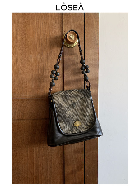 Black and brown leather shoulder handbag hanging on a wooden door
