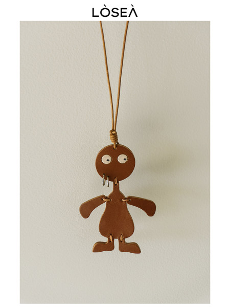 Brown leather character pendant necklace hanging against a plain wall