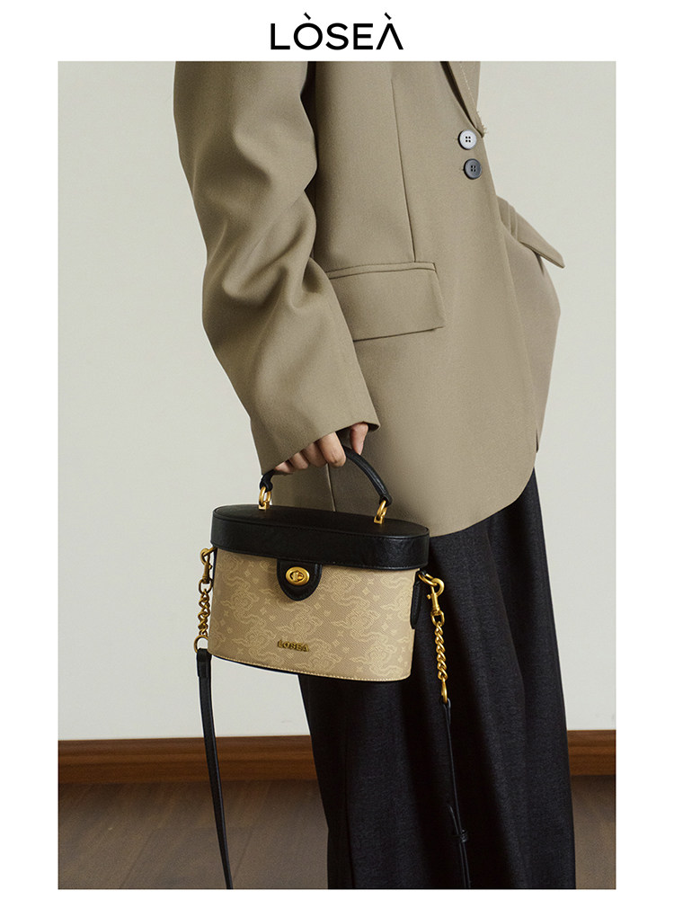 Beige and black structured handbag with gold hardware held by a model