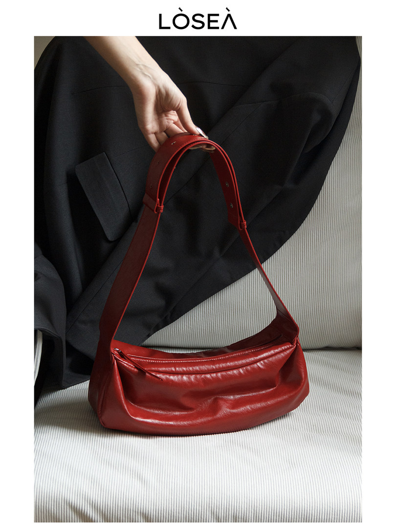 Red leather shoulder bag held by hand on a sofa