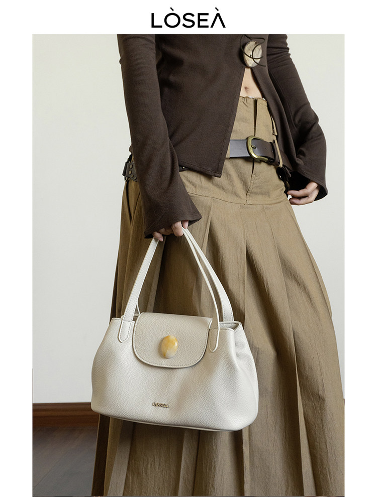 Cream handbag held by a model wearing a brown outfit
