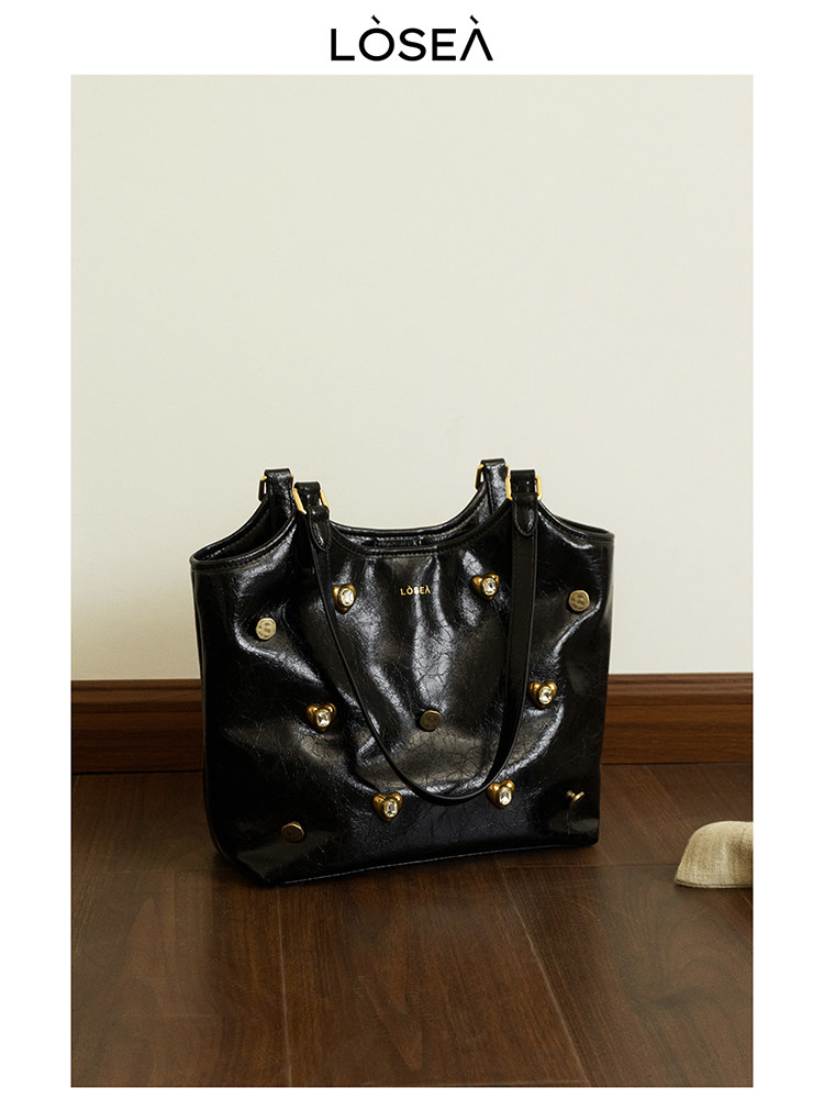 Black leather tote bag with gold-tone stud accents on a wooden floor