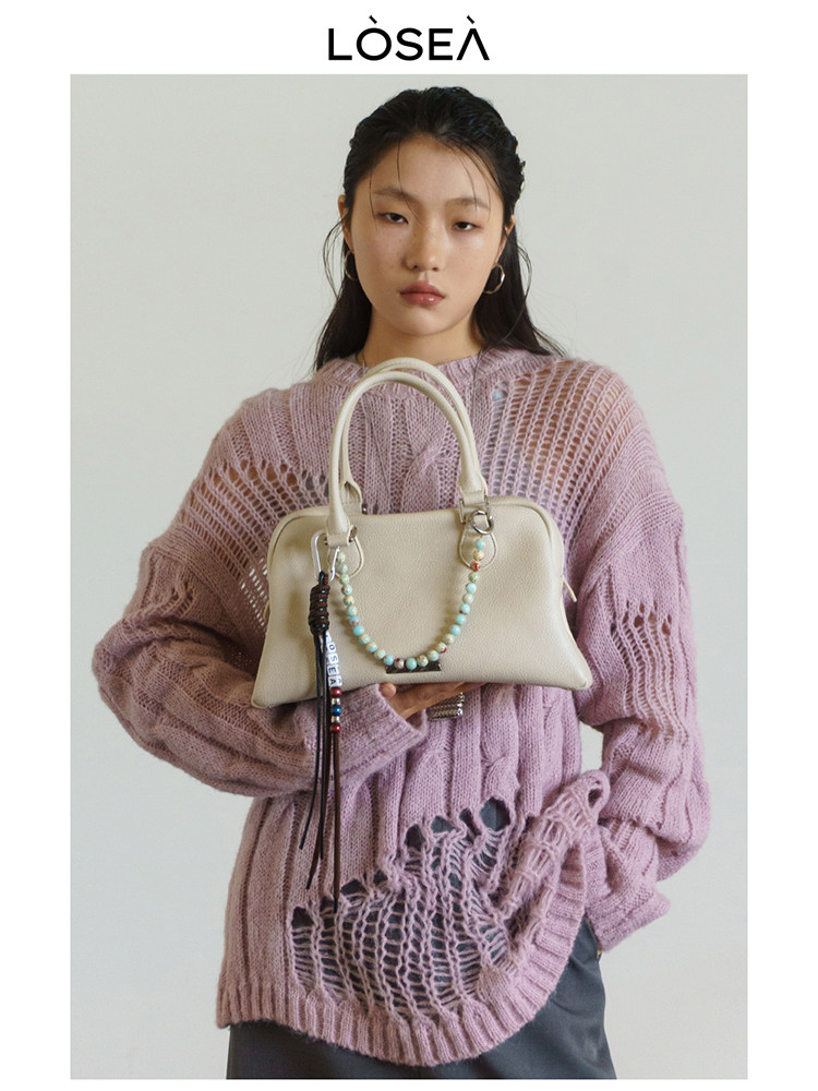 Model holding a cream handbag while wearing a pink chunky knit sweater