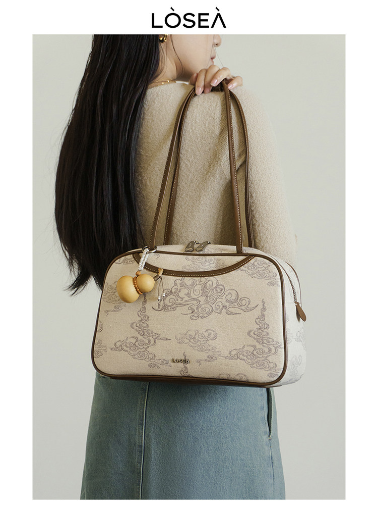 Beige patterned handbag with brown trim on a model's shoulder