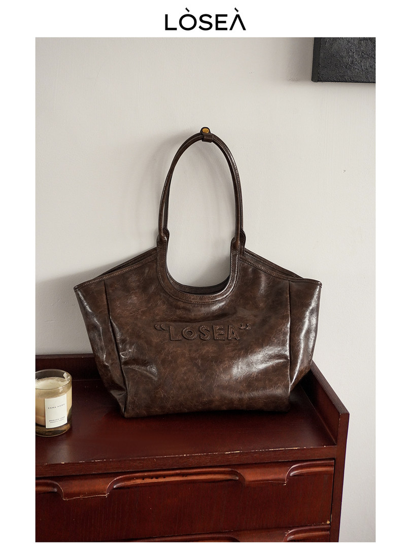 Brown leather tote handbag with long handles on a dresser
