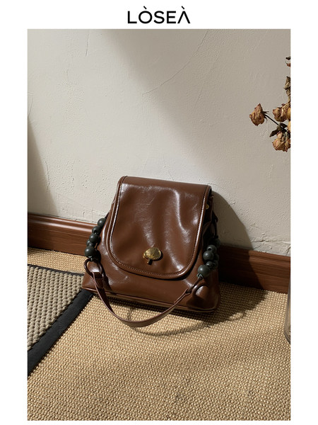 Brown leather handbag with bead strap displayed indoors