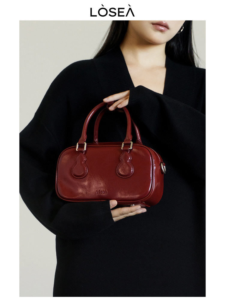Red leather handbag held by a woman in a black outfit