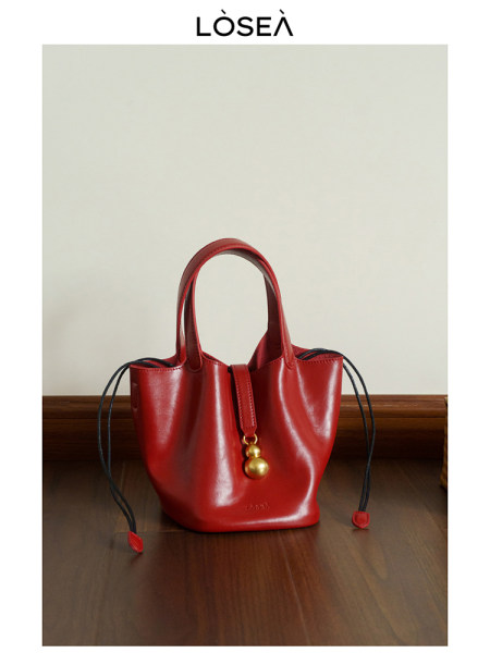 Red leather handbag with gold charm on a wooden floor