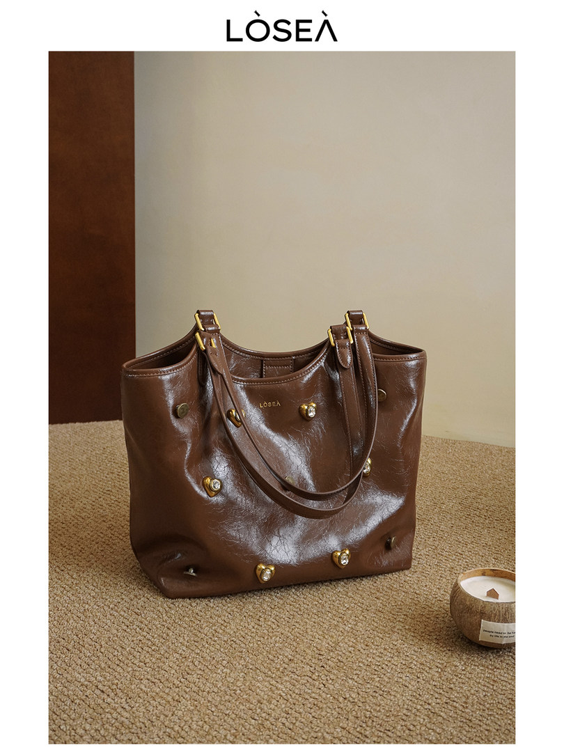 Brown leather tote handbag with gold hardware on a carpeted floor