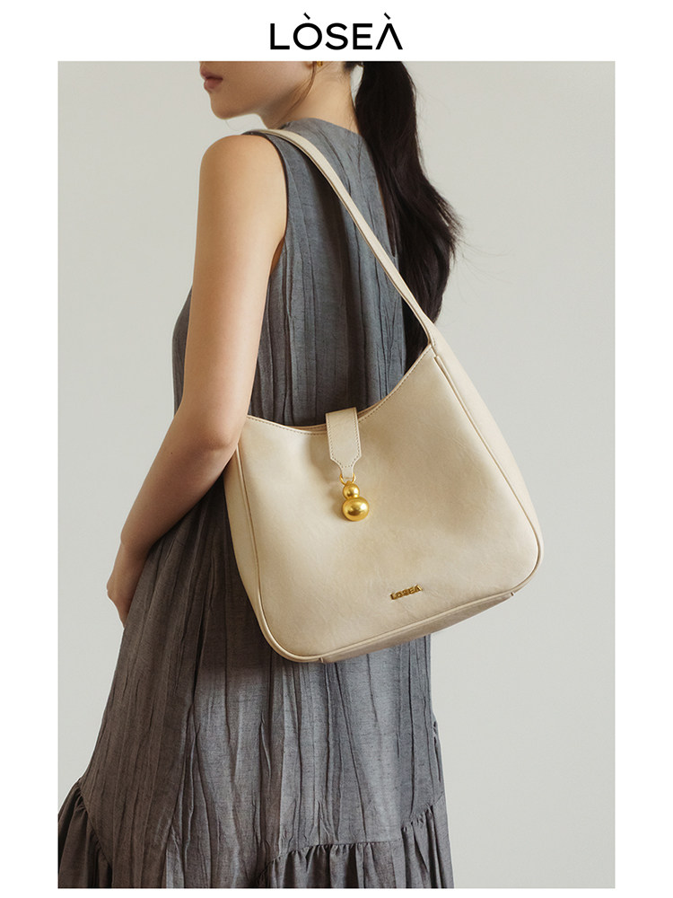 Cream shoulder handbag worn by a model in a gray dress