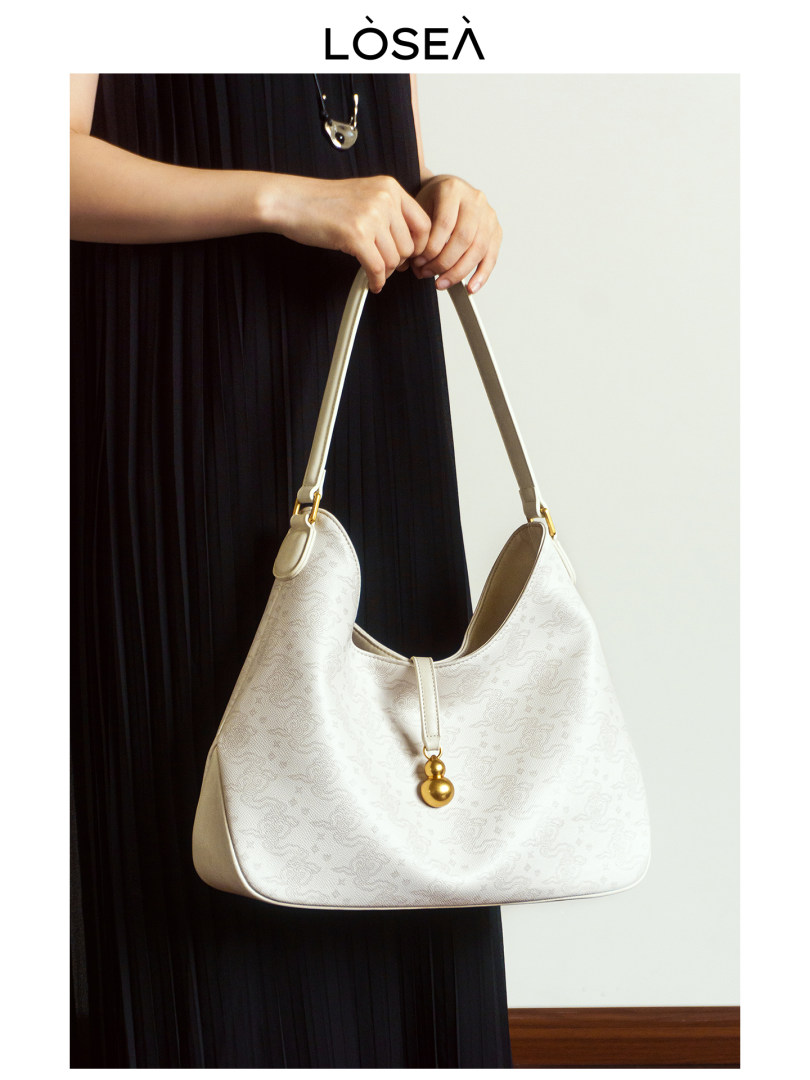 Cream shoulder handbag with gold charm held by a model