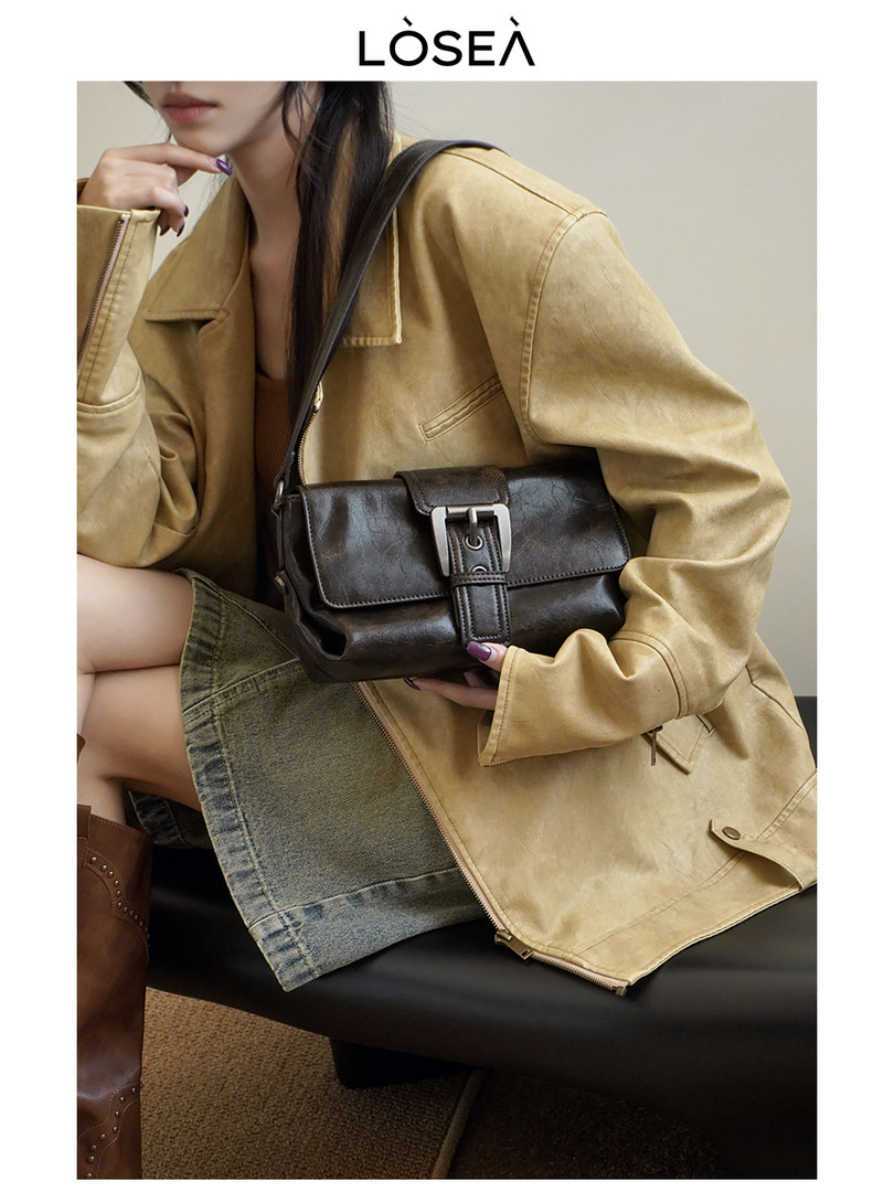 Model wearing a tan jacket and holding a dark brown leather shoulder bag